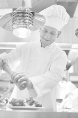 Mature chef using peppermill on salad in plate at restaurant