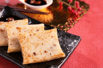 Chinese lunar new year food concept, Delicious turnip radish cake, local cuisine in restaurant with soy sauce on red background, close up, copy space
