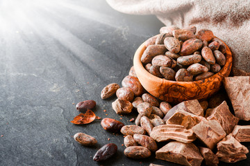 Cocoa raw beans in bowl and dark chocolate on black stone table.