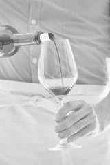 Black and white photo of waiter pouring red wine in wineglass at restaurant