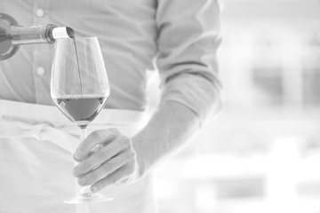 Black and white photo of waiter pouring red wine in wineglass at restaurant