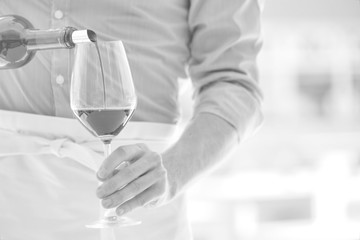 Black and white photo of waiter pouring red wine in wineglass at restaurant