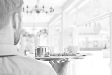 Young waiter serving coffee and cookies at restaurant