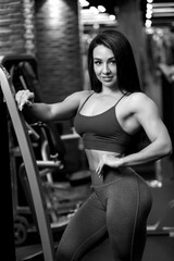 Fototapeta na wymiar Sexy fitness brunette girl is standing near training apparatus and posing BW