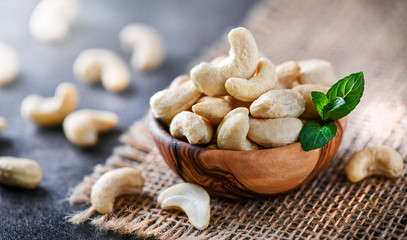 Cashew nuts in wooden bowl on dark black table with mint leaf on top. Raw cashews side view.