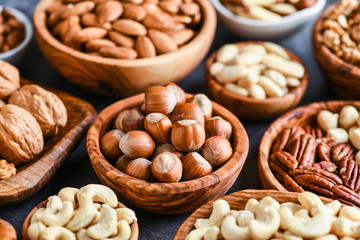 Obraz na płótnie Canvas Mix of nuts in wooden bowls on dark stone table top view. Walnuts, cashew, almond, pistachio, pecan, hazelnut, macadamia nut. Healthy various super food selection.