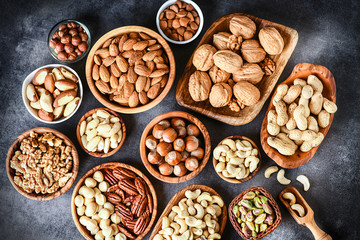 Mix of nuts in wooden bowls on dark stone table top view. Walnuts, cashew, almond, pistachio, pecan, hazelnut, macadamia nut. Healthy various super food selection.