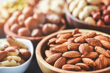 Mix nuts in wooden bowls on dark stone table. Almonds, pistachio, walnuts, cashew, hazelnut.