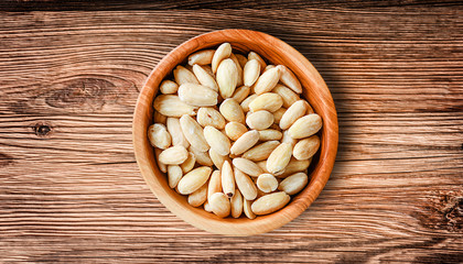 Pile of peeled almond in wooden bowl top view on rustic table. Almonds nuts is healthy food.