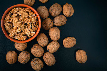 Pile of walnuts and peeled nuts in bowl. View from above.	