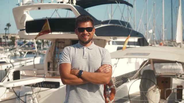 Man dressed in casual wear near yacht. Happy adult bearded yachtsman close-up portrait. Handsome sailor smiling during regata on a sea or river.