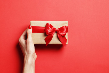 Christmas gift box in a female hand on a red background. Place for text.