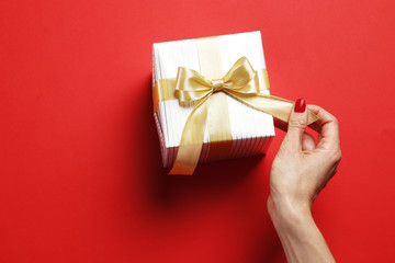 Festive gift box in a female hand on a red background. Place for text.