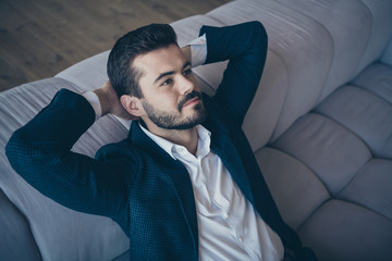 High angle view photo of handsome business guy sitting minded hands behind head on comfort sofa in apartment office building indoors wear formalwear costume