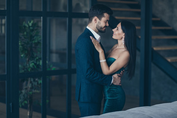 Profile photo of two famous trendy people couple rich guy and lady standing close looking eyes happily smiling romance date wear classy formalwear suit dress loft indoors