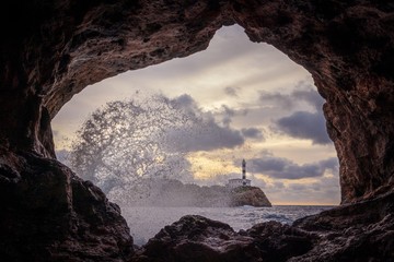 Portocolom lighthouse, natural stone cave, blue sea withwave and sea spray, Mallorca, Spain.