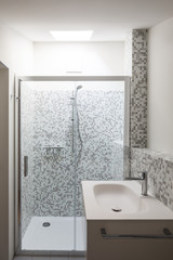 Bathroom renovated with mosaic of grey tiles. Washbasin, shower and skylight