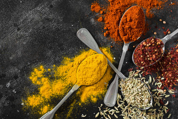 Spices in metal spoons on a black table