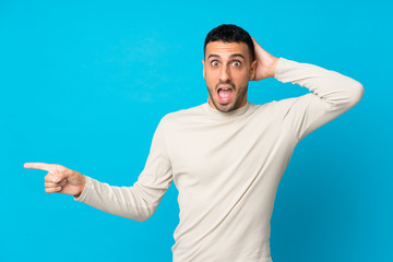 Naklejka premium Young man over isolated blue background surprised and pointing finger to the side