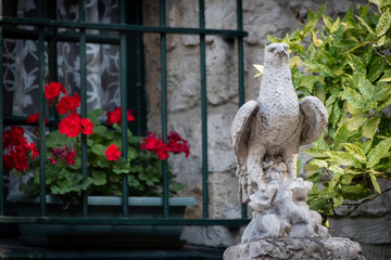 stone sculpture of a hawk with barred window and red geraniums in background