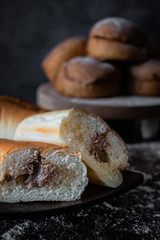 Bread with chocolate cream filling on a dark table with a stack of buns in the background