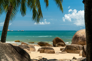 Tropical coast view with beach, stones and surrounding palm trees