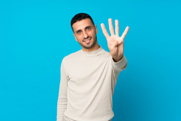 Naklejka premium Young man over isolated blue background happy and counting four with fingers