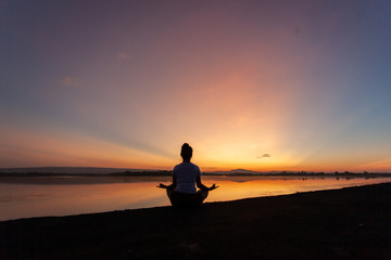 Fototapeta na wymiar Young woman in a meditating yoga pose overlooking the beautiful sunset. Mind body spirit concept.