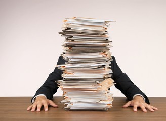 Young businessman hid behind with stack of papers on wooden table in room