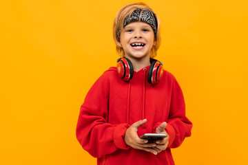 naughty schoolboy in a red hoodie with a phone in his hands, a boy in headphones on a background of an orange wall