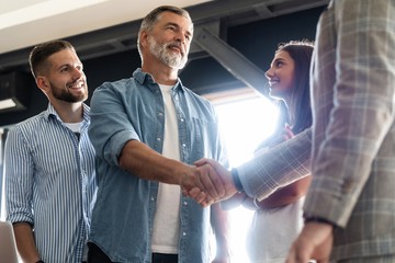 Welcome to our team! Business men in smart casual wear shaking hands while working in the creative office.