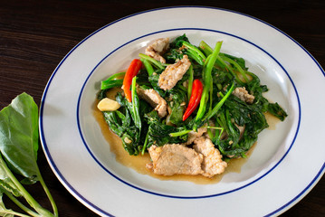 Stir fried kale with pork in white dish and fresh kale, Thai food