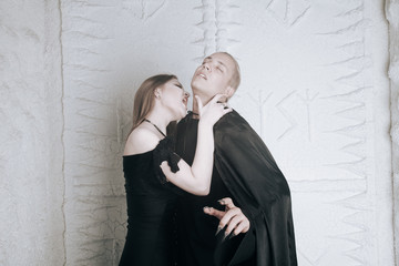 young vampire love couple in black halloween costumes ready for the party. man and woman bite and enjoy each other on white background.