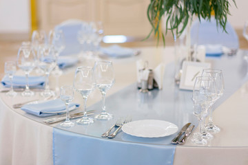 Wine glasses are on the table in the restaurant. White plates with blue tablecloths
