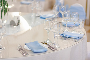 Wine glasses are on the table in the restaurant. White plates with blue tablecloths