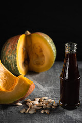 in the bottle, dark pumpkin oil is next to the cut pumpkin and seeds.
