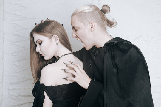 young vampire love couple in black halloween costumes ready for the party. man and woman bite and enjoy each other on white background.
