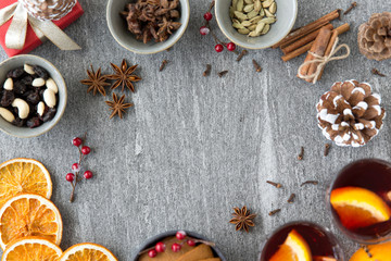 christmas, winter holidays and seasonal drinks concept - hot mulled wine, dry orange slices, raisins with pine cones and aromatic spices on grey background