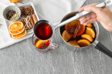 christmas and seasonal drinks concept - hand with ladle pouring hot mulled wine with orange slices...