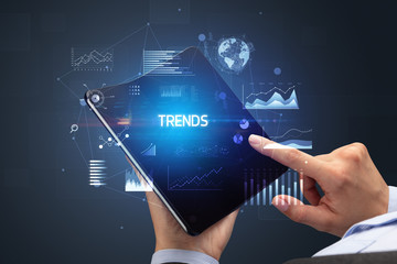 Businessman holding a foldable smartphone with TRENDS inscription, successful business concept