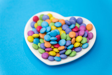 sweets, confectionery and valentine's day concept - candy drops on heart shaped plate over blue background