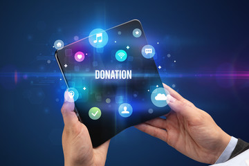 Businessman holding a foldable smartphone with DONATION inscription, social media concept