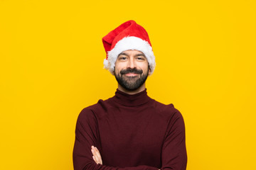 Man with christmas hat over isolated yellow background keeping the arms crossed in frontal position
