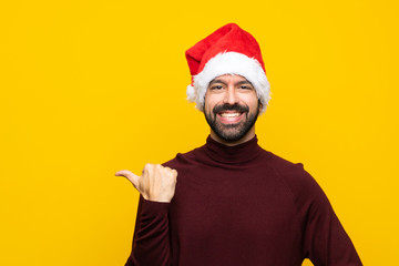 Man with christmas hat over isolated yellow background pointing to the side to present a product