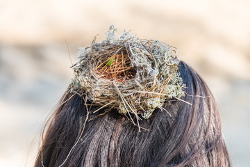 An empty nest made by birds from grass, branches and pine needles on the head of girl in the forest.