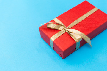holiday, greeting and surprise concept - christmas red gift box with golden bow on blue background