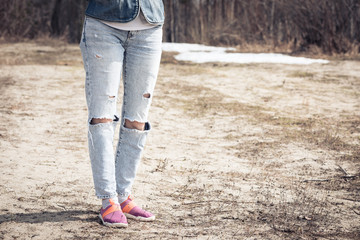 Slender legs of girl in holey jeans and summer sneakers to cool the body from the heat.