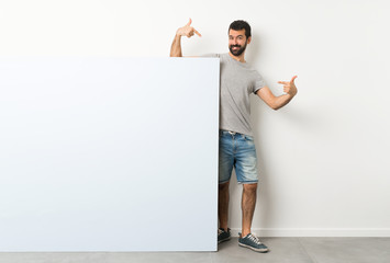 Young handsome man with beard holding a big blue empty placard proud and self-satisfied