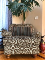 upholestered chair with large green plant in the corner of a room