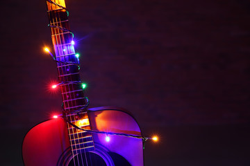 Acoustic guitar with Christmas lights against dark background